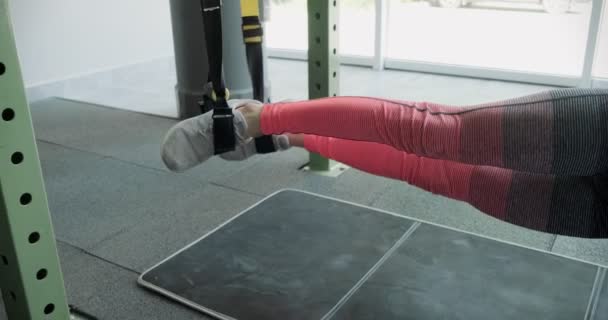 Красивая молодая женщина тренируется с фитнес-ремнями в тренажерном зале. Привлекательная женская тренировка — стоковое видео