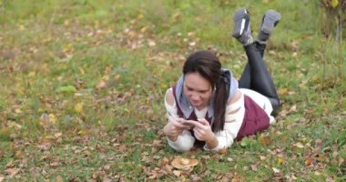 Mutlu kız parkta çim üzerinde yalan. Telefon fotoğrafları. Sarı yapraklar