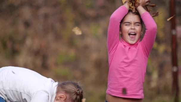 Två små glada flickor med blad i parken. Gula blad — Stockvideo