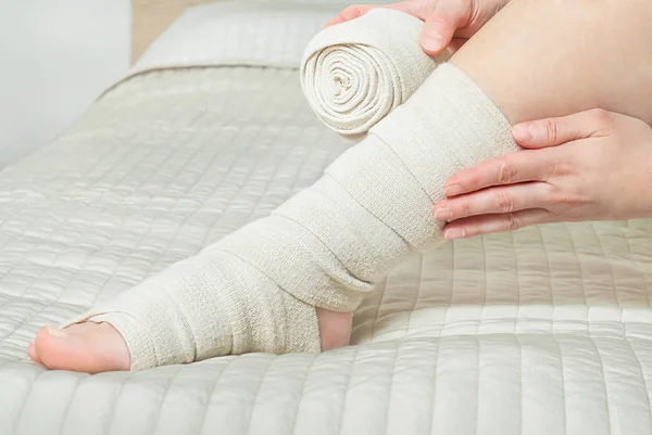 Woman applying elastic compression bandage as a thrombosis prevention after varicose surgery — Stock Photo, Image