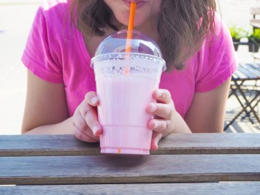 Kız yaz günü kafede saman ile çilek milkshake plastik cam tutan