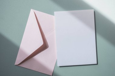 Boş beyaz tebrik kartı ya da mavi arka planda pembe zarf olan davetiye kartı. Sunum uydurma. Kopyalama alanı olan asgari modern biçim.