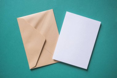 Beyaz boş selamlama ya da yeşil arka planda davetiye kartı ve zarf. Sunum uydurma. Düz konum, kopyalama alanı olan üst görünüm. En küçük arkaplan