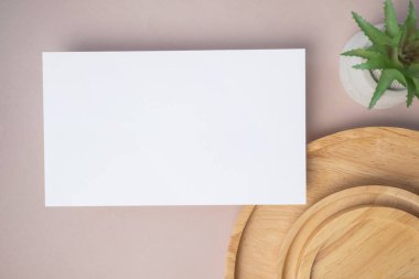 Empty white blank greeting or invitation card, cactus, wooden plate on beige background. Mock up presentation. Minimal modern style with copy space.