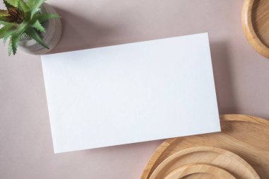 Empty white blank greeting or invitation card, cactus, wooden plate on beige background. Mock up presentation. Minimal modern style with copy space.