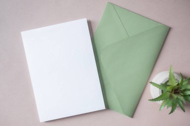 Empty white blank greeting or invitation card, green envelope, cactus on beige background. Mock up presentation. Minimal modern style with copy space