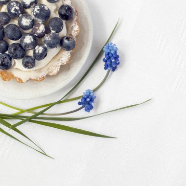 Vanilyalı krema bölümü plaka yakın çekim, zarif bir sonraki mavi çiçekler, beyaz peçete ile taze yaban mersini turtası. Lezzetli ve romantik berry tatlı, kopya alanı, kare yaz