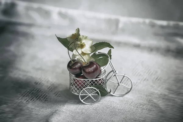 Miniatur-Spielzeugwarenkorb, Trolley Nahaufnahme mit reifen Kirschen, Blumen, Vintage-Hintergrund. Konzept Landwirtschaft, gesunde Ernährung, Entgiftung, Vitamine, Ernährung — Stockfoto