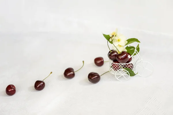 Sweet ripe cherry spill out of miniature toy, trolley closeup on light background, flowers, leaves, top view. Concept of healthy food, detox, vitamins, dieting, summer — Stock Photo, Image