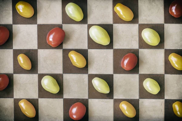 Two kinds of multicolored ripe cherries tomatoes on a chessboard, top view. Vintage background. Concept of healthy food, detox, vitamins, dieting