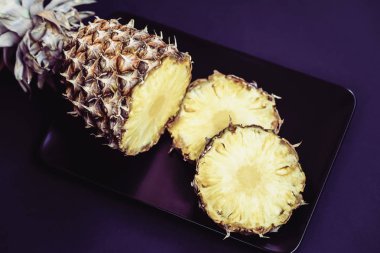 Kokteyller, şemsiyeler için süslemeler ile siyah bir plaka üzerinde olgunlaşmış ananas dilimleri. Koyu mor arka plan