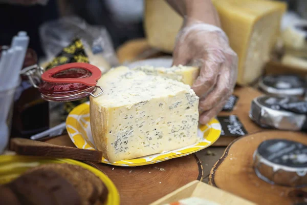Corte pedaços de queijo genuíno, mercado agricultor. Pedaço de queijo com mofo azul e mão do vendedor, balcão de mercado, cena real no mercado de alimentos — Fotografia de Stock