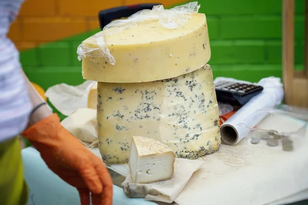 Pedaços de queijo com mofo azul e mãos de vendedor, balcão de mercado. Produtos gastronómicos delicados no balcão do mercado, cena real no mercado alimentar — Fotografia de Stock