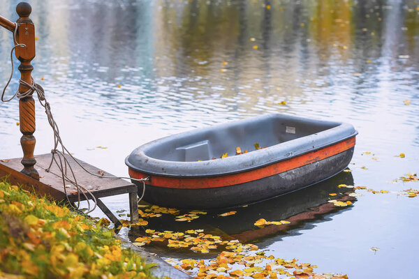 Moored boat in the autumn pond. Autumn scene, fallen yellow leaves on the shore, picturesque colors of nature, natural background, real scene, seasonal mood concept