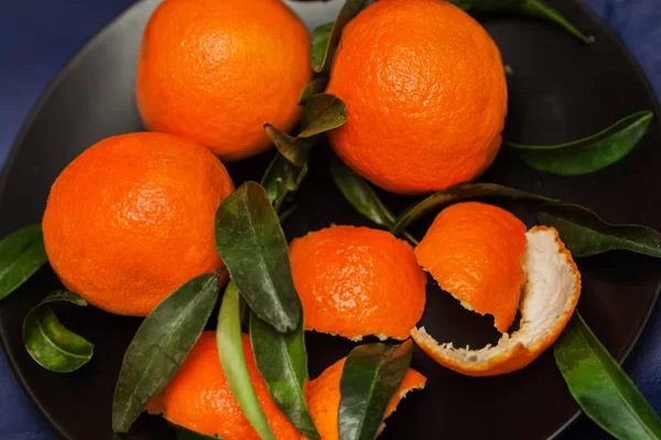 Tangerinas laranja maduras com folhas verdes em placa em preto, vista superior. Chave baixa. Conceito de nutrição saudável, dieta, desintoxicação. Foco seletivo — Fotografia de Stock