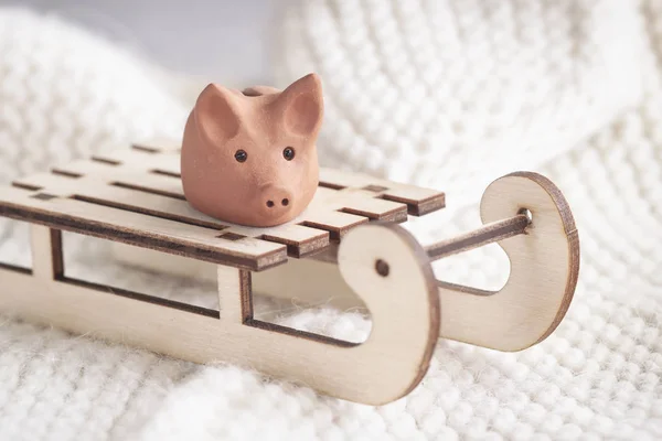 Symbol of the year by the horoscope, small clay pig on a wooden sled on knitted sweater