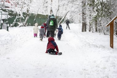 Açık hava oyunları, kış eğlence, tanınmayan küçük çocuklar anaokulu, karlı park, bir çocuk düştü, aktif yaşam tarzları elinde tutan yürüyüş öğretmenleri ile birkaç