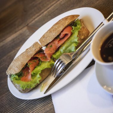Beyaz tabak taze sağlıklı sandviç somon ve yeşil marul, çatal bıçak takımı, kahve ile. Sağlıklı diyet kahvaltı. Çapraz üstten görünüm