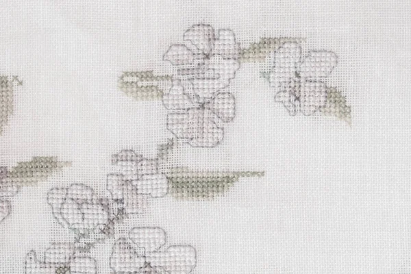 Fragment of a colorful cross-stitch embroidery, flower summer ornament on cotton canvas