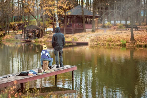 Adult and child on a wooden pier, fishing bridge. Autumn park. Fallen leaves, sunny day, natural background. — Stock Photo, Image