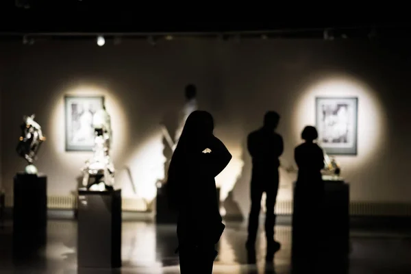 Silhouettes of unrecognizable people, visitors to an art gallery, a museum with paintings, selective focus