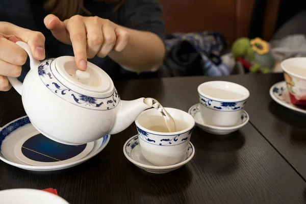 Teapot in the hands of a girl pouring green tea into beautiful chinese cups — Stock Photo, Image
