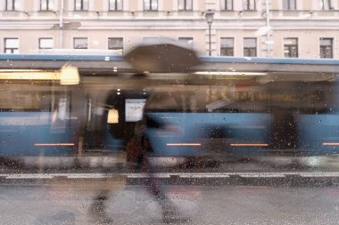 Şemsiyenin altındaki insan silueti, otobüse binen şehir caddesi pencere camındaki yağmur damlalarından görülebilen bulanık hareket. Mevsimler, hava, şehir konsepti