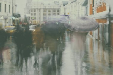 Yağmurlu bir akşamda şehir caddesinde şemsiyelerin altında aceleyle ilerleyen bulanık insanların soyut arkaplanı, empresyonizm tarzında. Kasıtlı hareket bulanıklığı