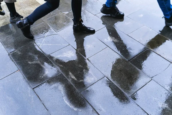 Reflexión borrosa piernas y sombras, siluetas de la gente en la acera mojada, en un charco de gente caminando sobre una lluvia — Foto de Stock