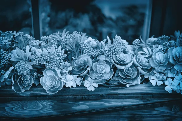 Mix types succulents and flowers on the windowsill on facade of the house, blue green background