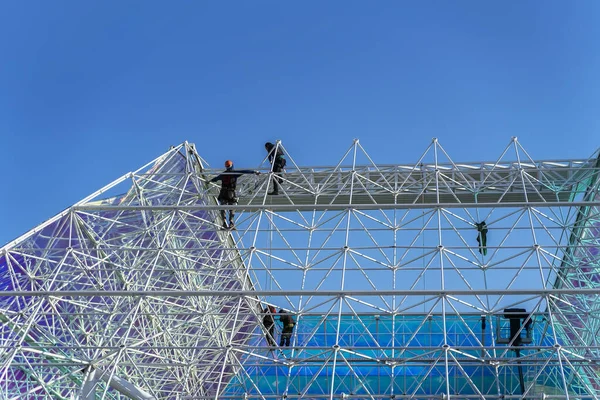 Malá část velké vysoké stavební konstrukce se siluetami dělníků, geometrickou konstrukcí, ocelovým rámem. Moderní pozadí — Stock fotografie