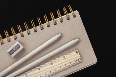 Tahta kırtasiye malzemesi, spiralleri ve koyu arkaplanı olan bir defterin üzerinde duruyor. Okula dönüş kavramı, eğitim