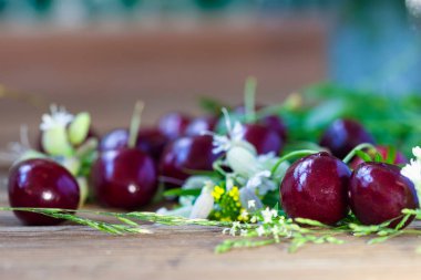 Büyük olgun kiraz meyveleri, ahşap arka planda çayır çiçekleri, bokeh ve seçici odak, mevsimsel konsept, kır hayatı, sağlıklı beslenme, yaz hasadı