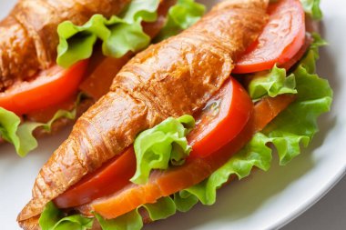 Füme somonlu kruvasan sandviç, kırmızı domates ve yeşil salata yakın plan, yüksek açı, sağlıklı kahvaltı, balık yemi.