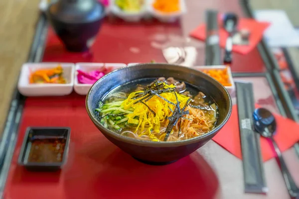 Udon erişteli Asya usulü çorba, et dilimleri, masanın üstündeki kasede yakın plan sebzeler, üst manzara. Seçici odak