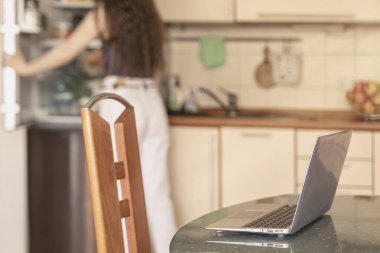 Defter evdeki mutfak masasında, yemek molasında tanınmayan bir kız buzdolabından yemek alıyor. Uzaktan çalışma anlayışı, ev ofisi, yaşam tarzı