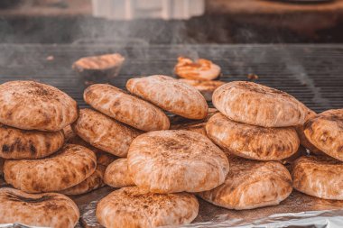 Izgaraya yığılmış taze pişmiş düz ekmekler, dumanlı kiraz izleriyle birlikte altın kahverengi ve kırsal. Düz ekmek hazırlama ve geleneksel sokak yemekleri kavramı