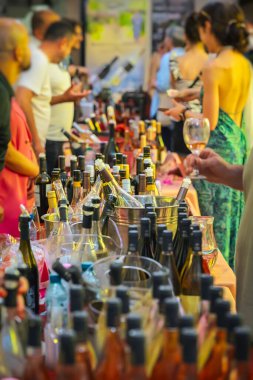 Wine bottles displayed on table at Wine Festival with people tasting and chatting in background, holding glasses. Concept of wine tasting, celebration, social event, fest lifestyle