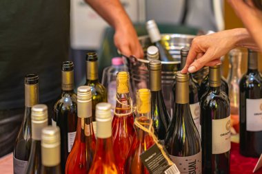 KAZANLAK, BULGARIA - JUNE 07, 2025: Closeup of wine bottles on table with female hand choosing one during tasting event, surrounded by people. Concept of wine tasting, selection, gourmet drinks