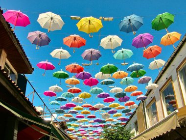 Açık güneşli bir caddede açık havada mavi gökyüzüne karşı çok renkli şemsiyeler.