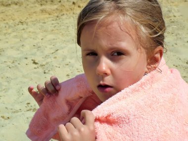 Battaniyeyle kaplanmış küçük bir kız kumlu bir plajın arka planında.