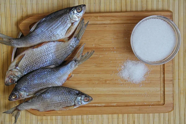 Dried salted river roach fish and coarse sea salt on a wooden board.
