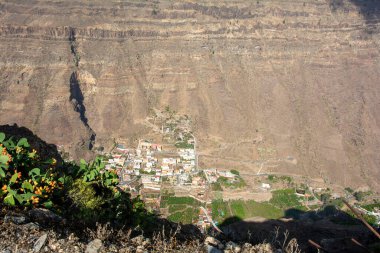 İspanya 'nın Kanarya Adası' ndaki vadide küçük bir köye sahip dağlar. Mavi gökyüzü ve bulutlarla kaplı.