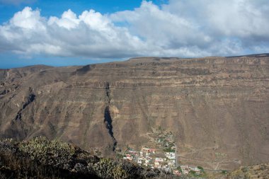 İspanya 'nın Kanarya Adası' ndaki vadide küçük bir köye sahip dağlar. Mavi gökyüzü ve bulutlarla kaplı.