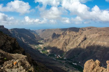 İspanya 'nın Kanarya Adası' ndaki vadide küçük bir köye sahip dağlar. Mavi gökyüzü ve bulutlarla kaplı.