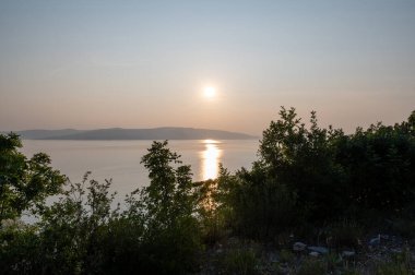 Hırvatistan, Avrupa 'da denizde gün batımı, arka planda Krk adası ve önde ağaçlar