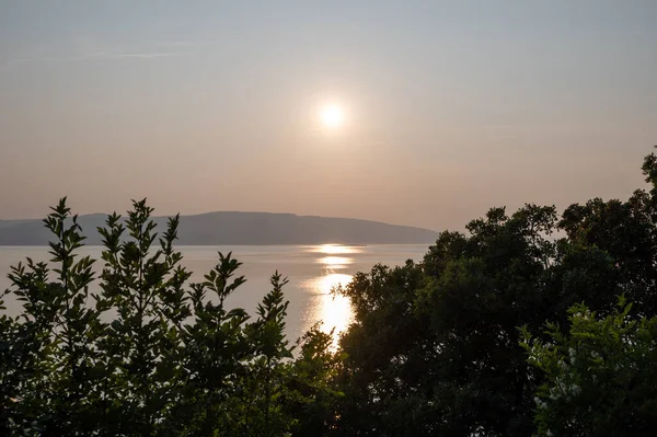 Hırvatistan, Avrupa 'da denizde gün batımı, arka planda Krk adası ve önde ağaçlar