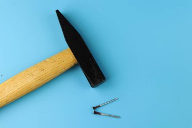 Bir küçük siyah demir çekiç ve mavi kağıt üzerinde yalan iki pas çivi. El ile çalışma