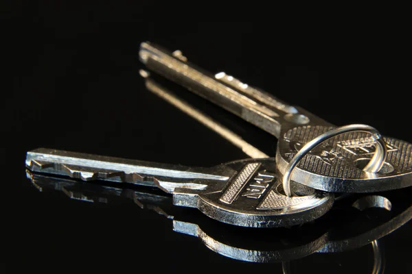 A two silver keys for opening doors connected by metal ringlet on the black background