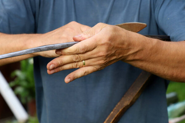Старик точит стальной край косы влажным камнем. Нужен острый край
